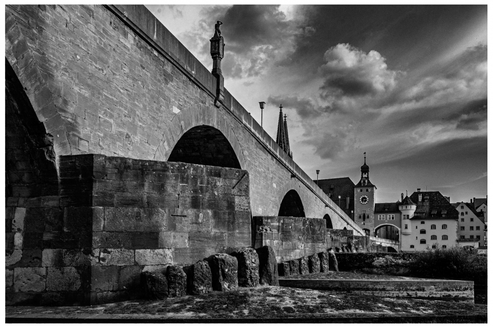 Historische steinerne Brücke mit Bögen, Fluss, traditionelle Gebäude, Uhrturm, wolkiger Himmel, © Klaus Gruber | dolphin photography