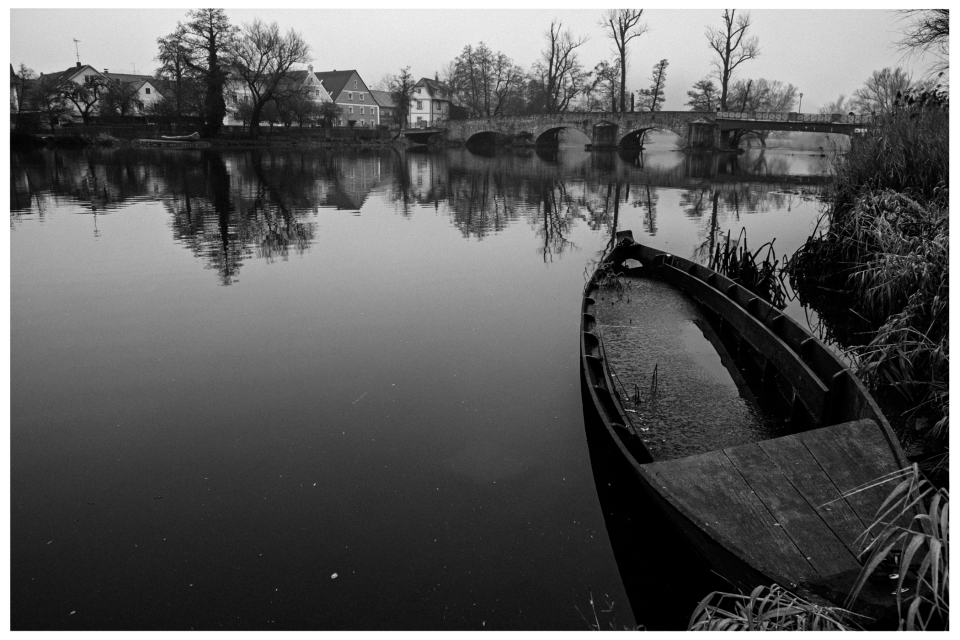 Ruhiger Fluss mit alter Bootsanlegestelle, steinerne Brücke und Häuser im Hintergrund, © Klaus Gruber | dolphin photography