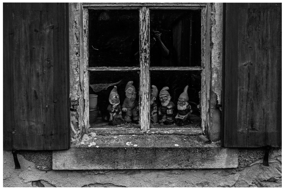 Verwitterte Fensterbank mit Gartenzwergfiguren hinter abgenutzten Holzläden und gealtertem Glas, © Klaus Gruber | dolphin photography
