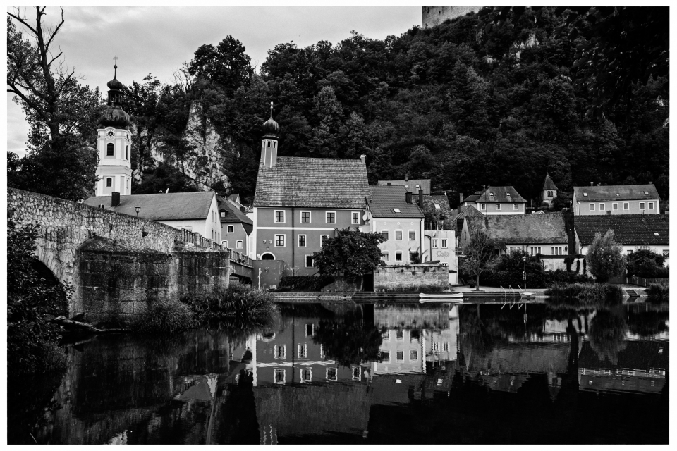 Dorf am Fluss mit Kirche, Zwiebelturm und bewaldeten Hügeln, Gebäude spiegeln im Wasser, © Klaus Gruber | dolphin photography