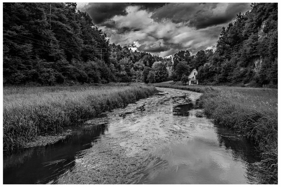 Fluss durch bewaldete Landschaft mit Haus am Ufer und bewölktem Himmel, © Klaus Gruber | dolphin photography
