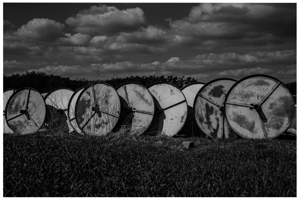 Gruppe großer, rostiger Kabeltrommeln auf grasbewachsenem Feld unter wolkigem Himmel, © Klaus Gruber | dolphin photography