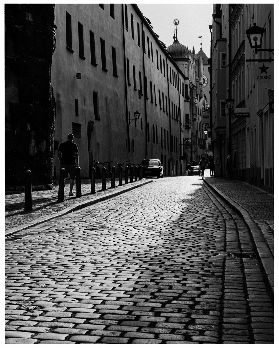 Gepflasterte Straße zwischen hohen Gebäuden mit Türmen, Menschen und Fahrrädern am Straßenrand, © Klaus Gruber | dolphin photography