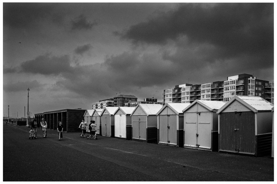 Reihe von Strandhütten an einer Promenade, Mehrfamilienhäuser im Hintergrund, wolkiger Himmel, © Klaus Gruber | Fotograf Fürth