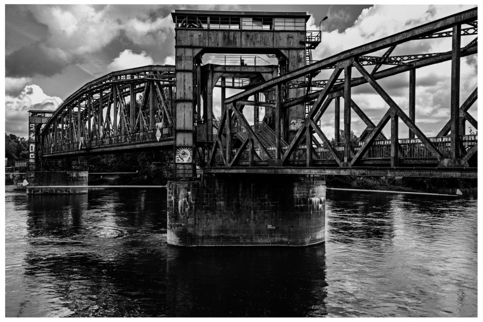 Stählerne Brücke mit komplexen Metallstreben überquert Fluss, Himmel voller Wolken, © Klaus Gruber | Fotograf Fürth