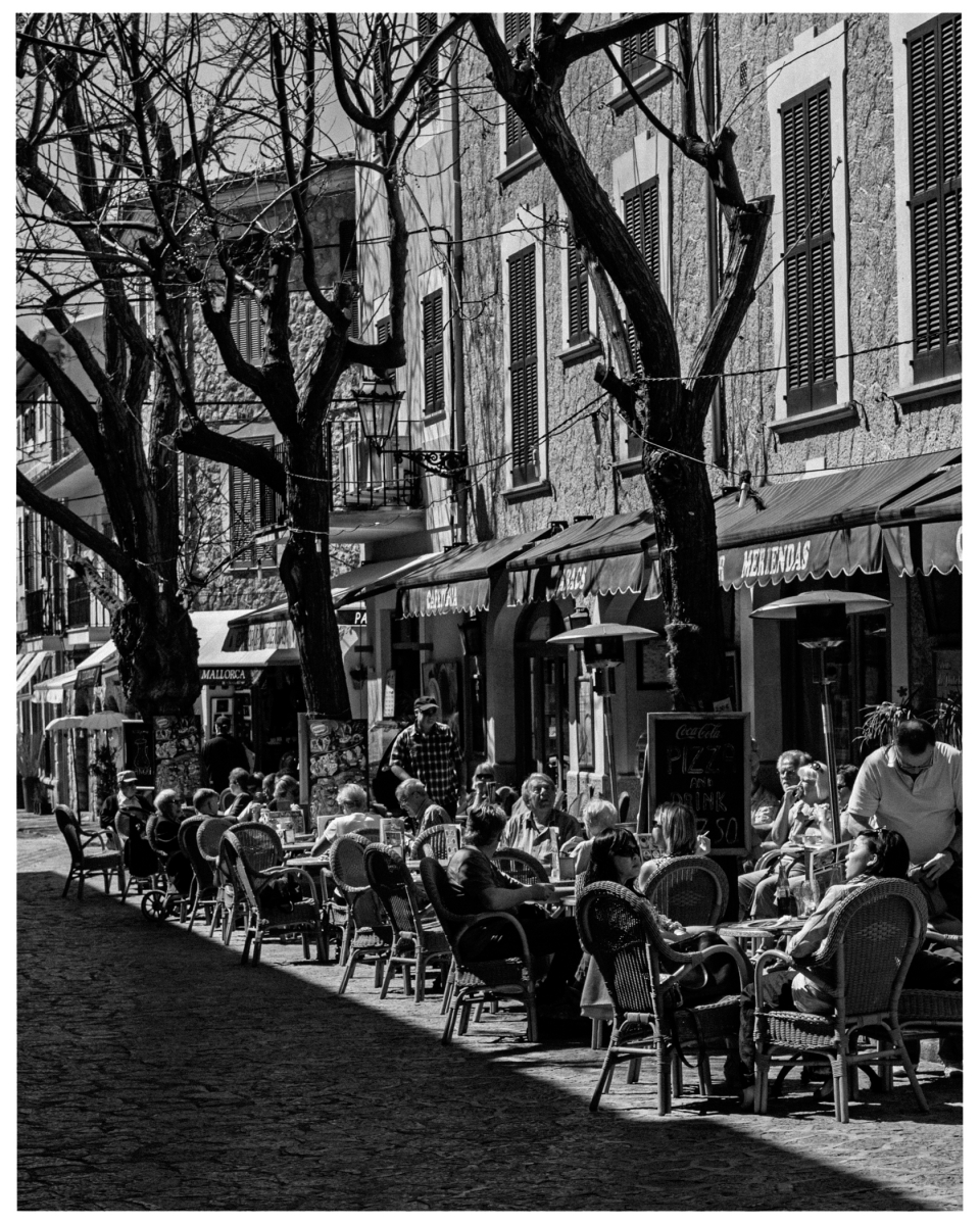 Menschen in Straßencafé, umgeben von alten Häusern und Bäumen mit langen Schatten, © Klaus Gruber | Fotograf Fürth