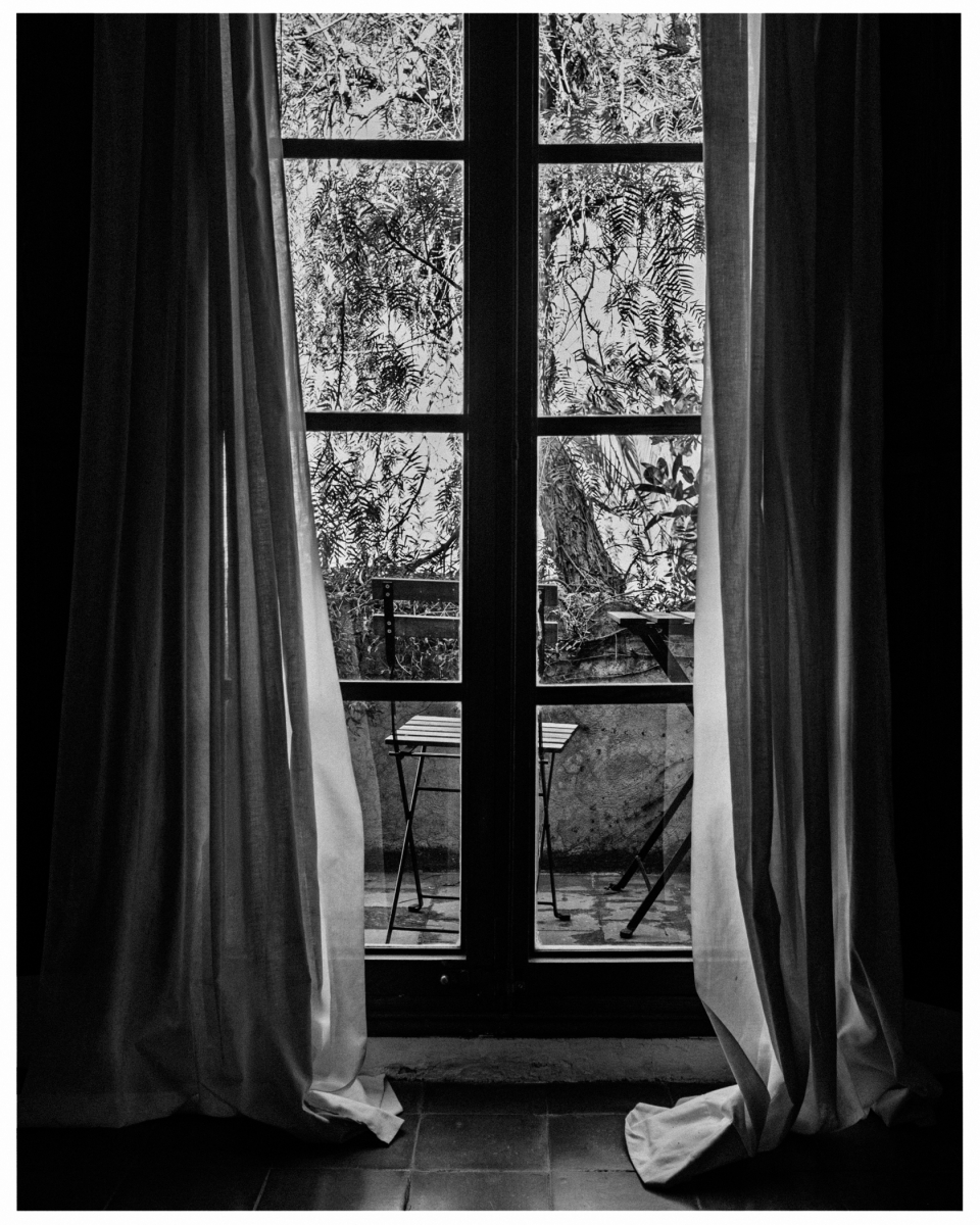 Fenster mit offenen Vorhängen zeigt Balkon mit Tisch, Stuhl und Pflanzen draußen, © Klaus Gruber | Fotograf Fürth
