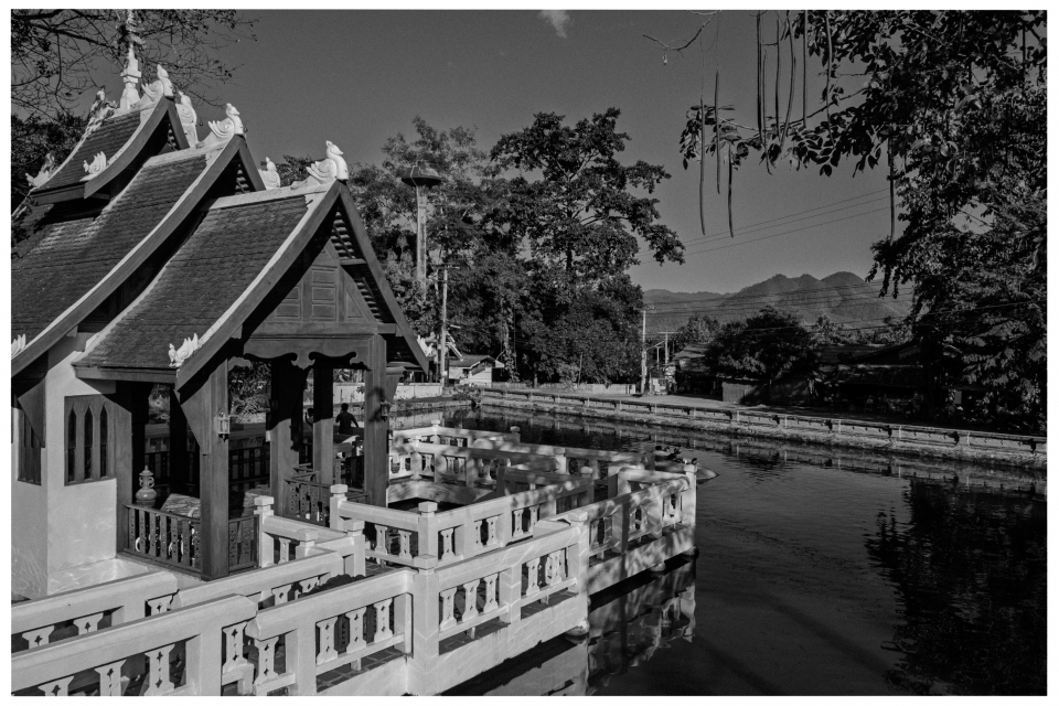 Traditionelles Gebäude am Flussufer, umgeben von Bäumen, Bergen im Hintergrund, © Klaus Gruber | Fotograf Fürth