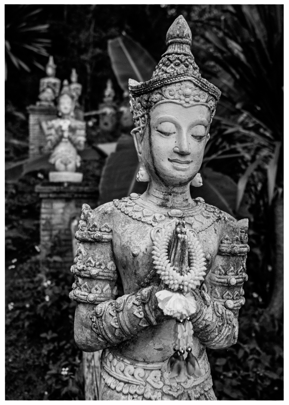 Steinerne Statue in Gebetspose mit weiteren ähnlichen Skulpturen im grünen Hintergrund, © Klaus Gruber | Fotograf Fürth