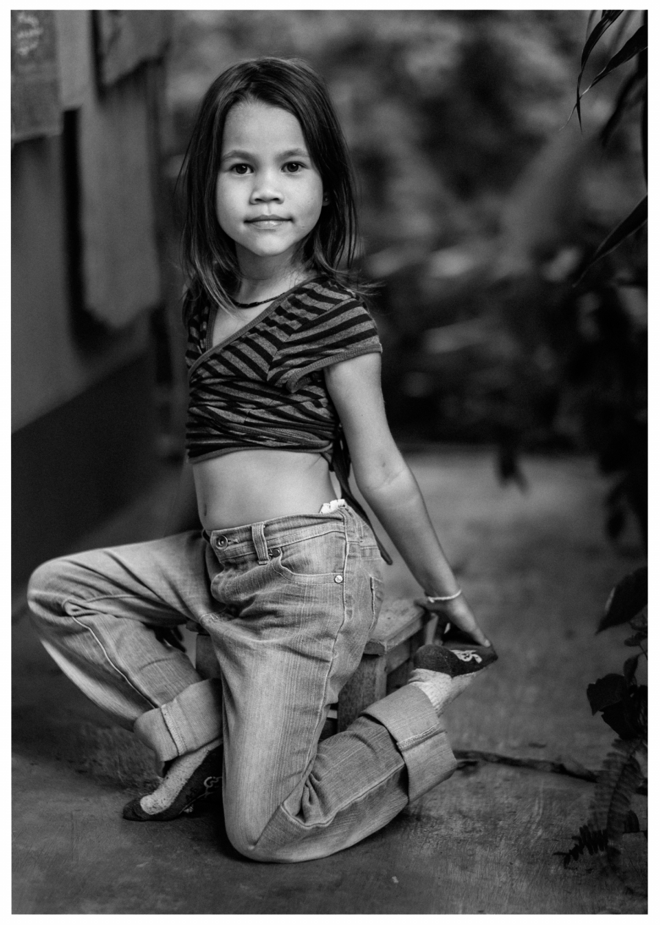 Mädchen in gestreiftem Oberteil und Jeans kniet in unscharfem Innenraum, Schwarzweißfoto, © Klaus Gruber | Fotograf Fürth