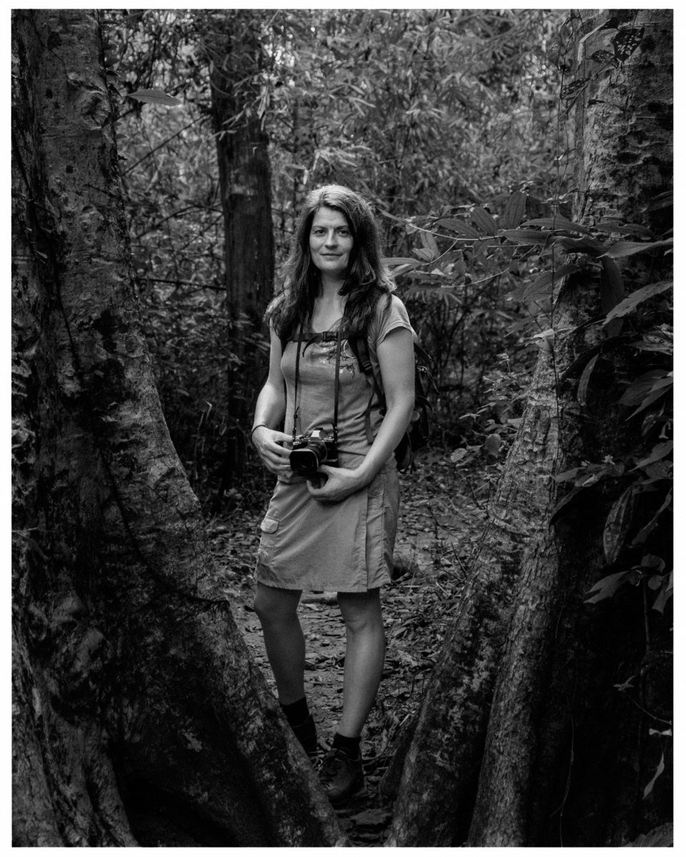 Frau im Wald, umgeben von Bäumen, hält Kamera in den Händen, © Klaus Gruber | Fotograf Fürth